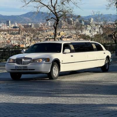 Una limusina blanca está estacionada al costado de la carretera frente a una ciudad.