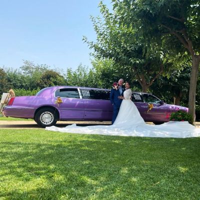 Una novia y un novio posan para una foto delante de una limusina violeta.
