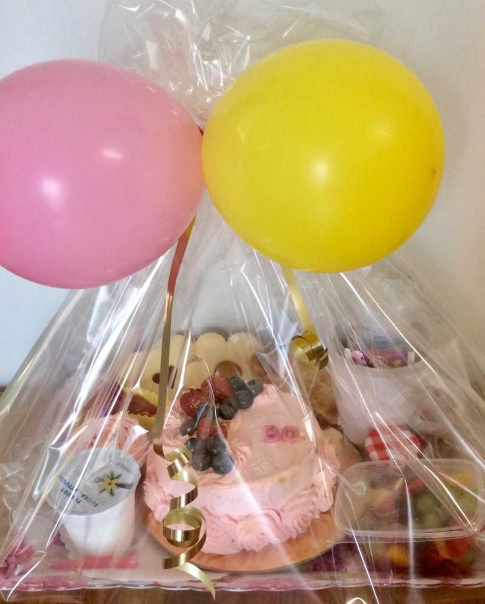Una torta avvolta nella plastica con due palloncini rosa e gialli
