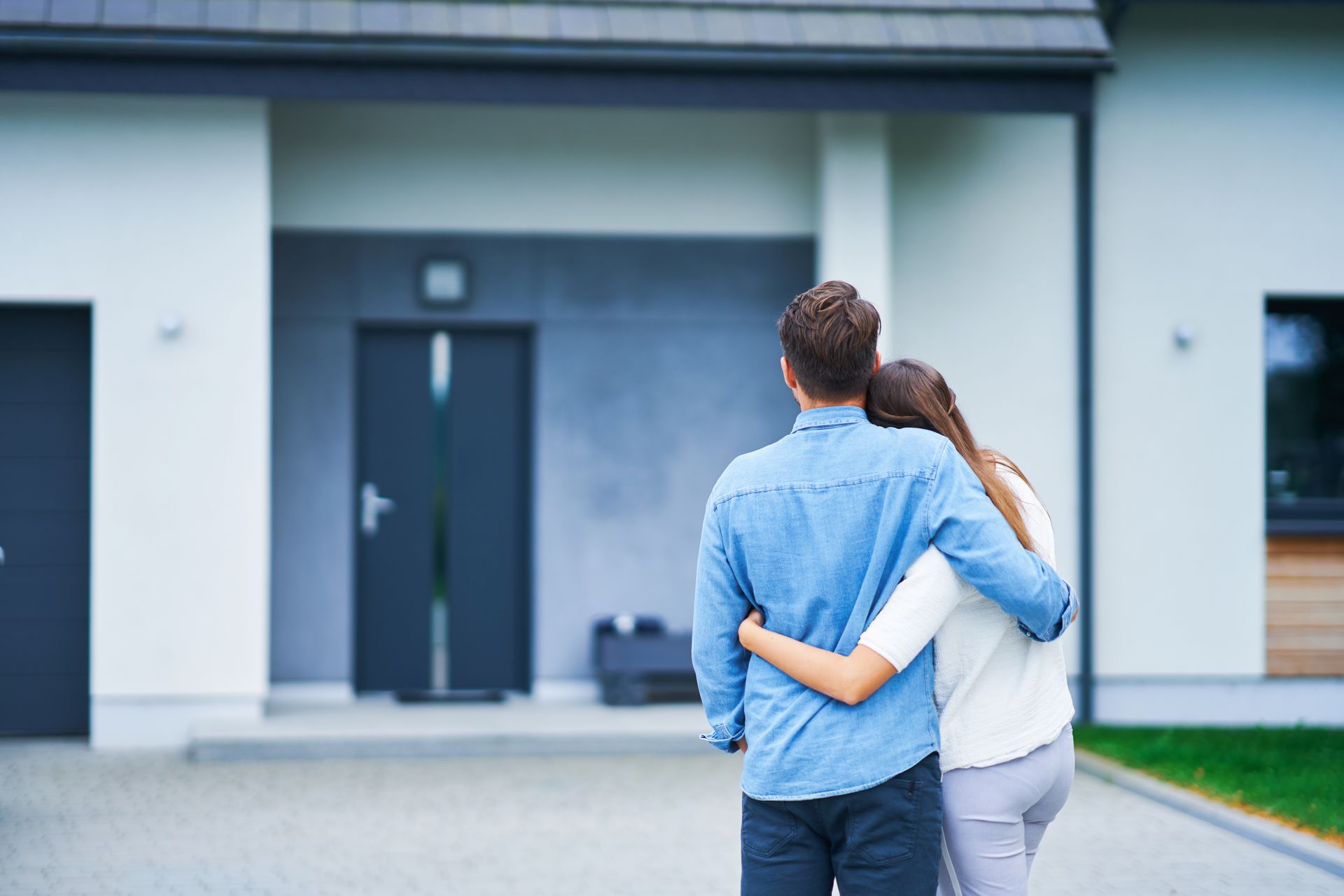 Jeune couple s'enlaçant devant la porte de leur nouvelle maison neuve