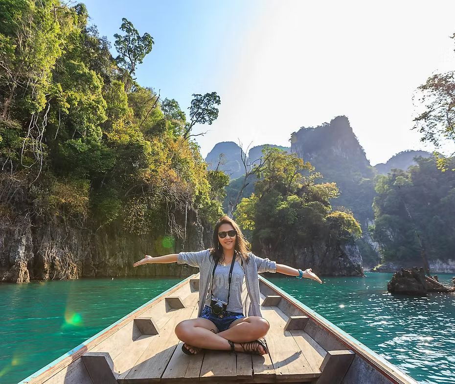 A woman is sitting in a boat on a lake with her arms outstretched.