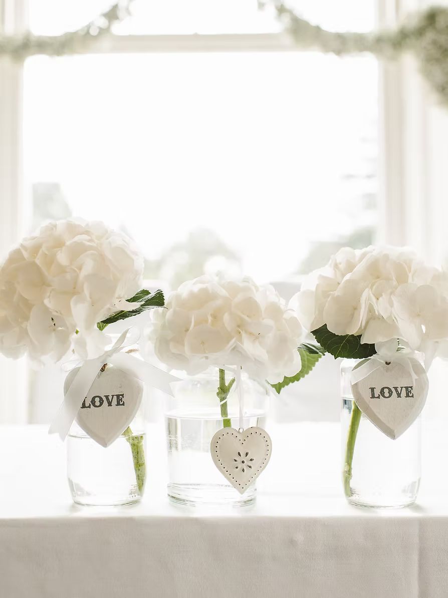 Three vases filled with white flowers and hearts on a table.