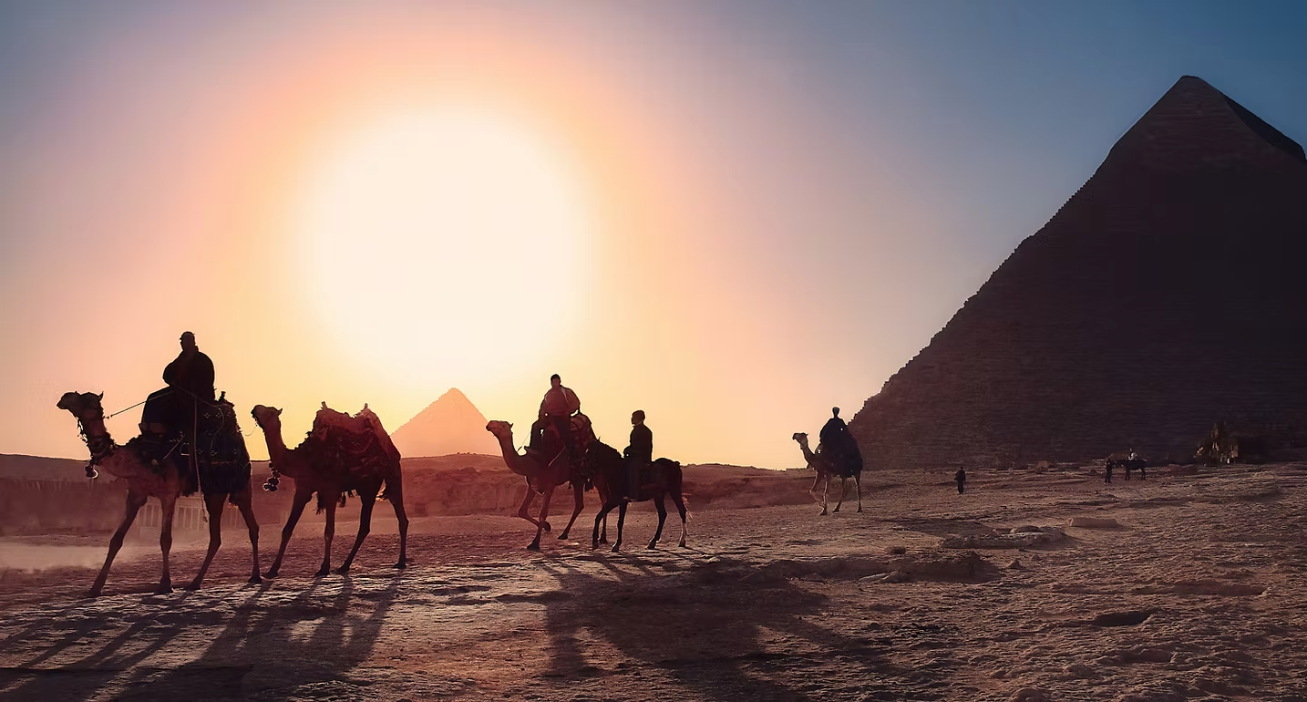 A group of people are riding camels in front of the pyramids.