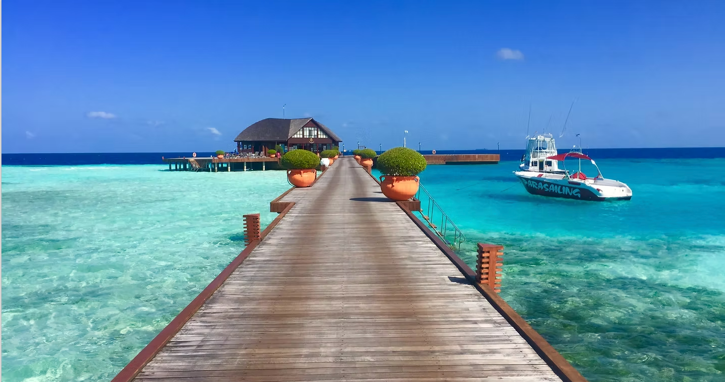 A wooden pier leading to a small island in the middle of the ocean.