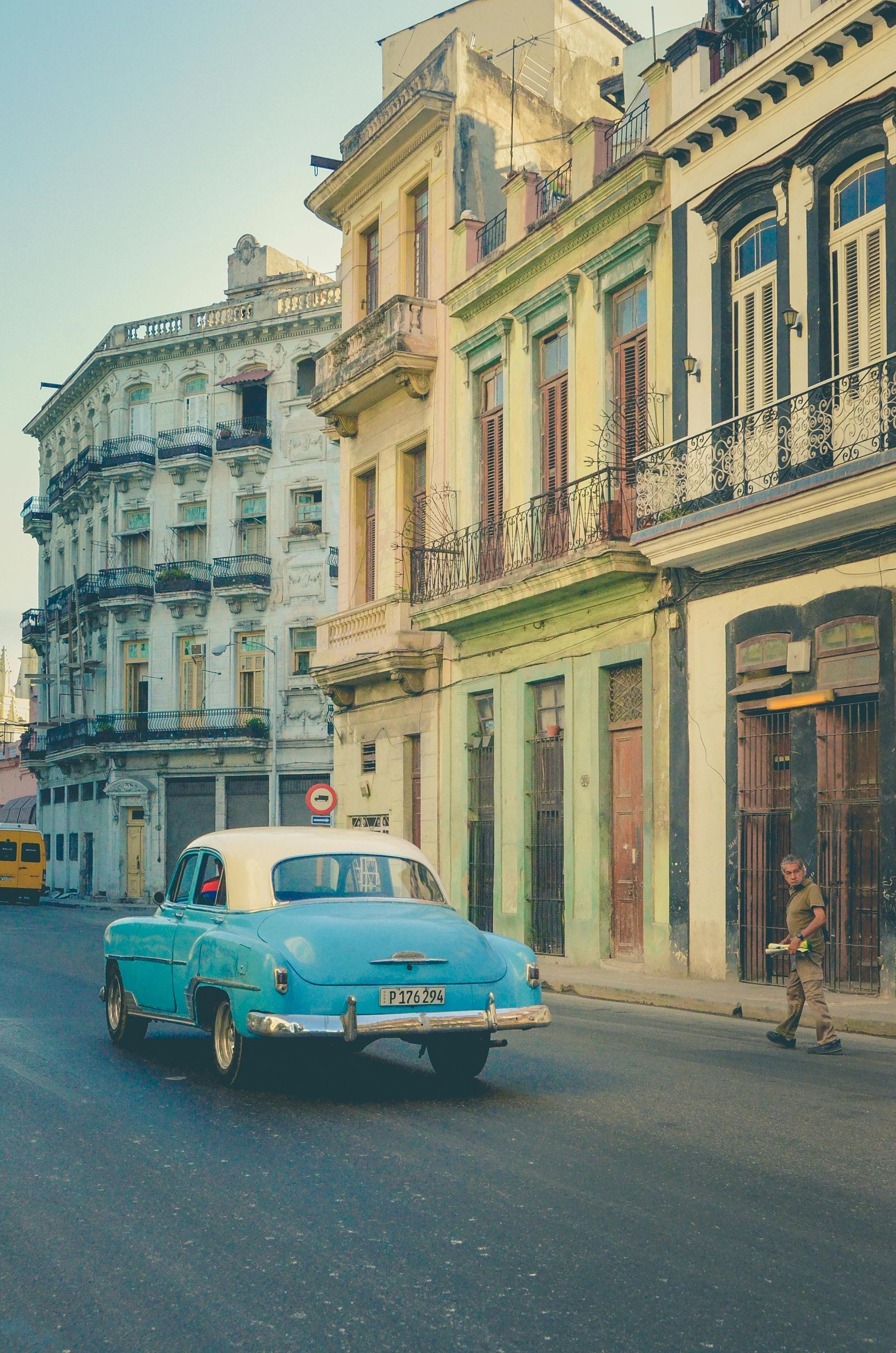 A blue and white car is driving down a city street.