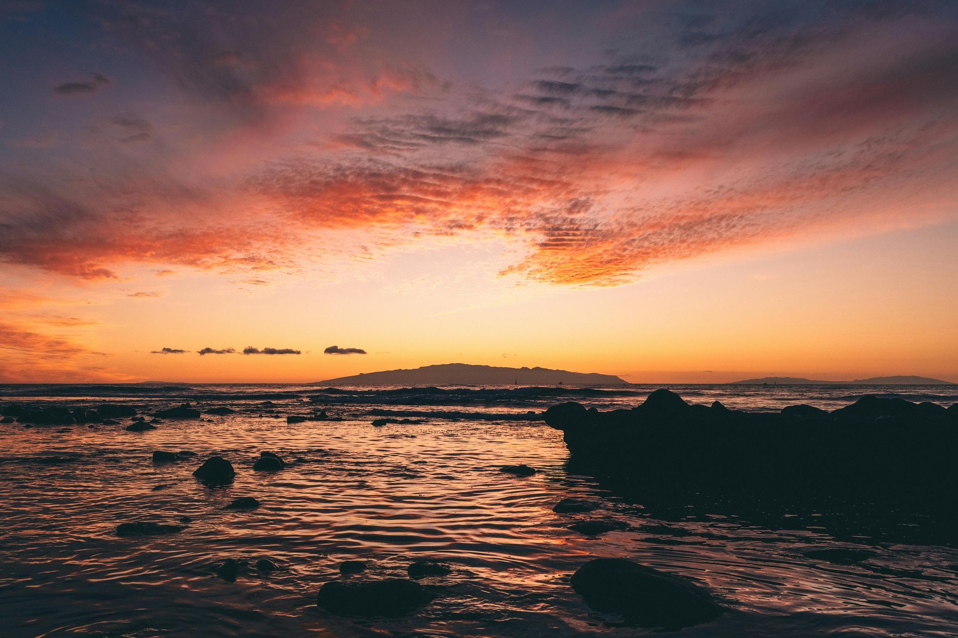 A sunset over a body of water with rocks in the foreground.