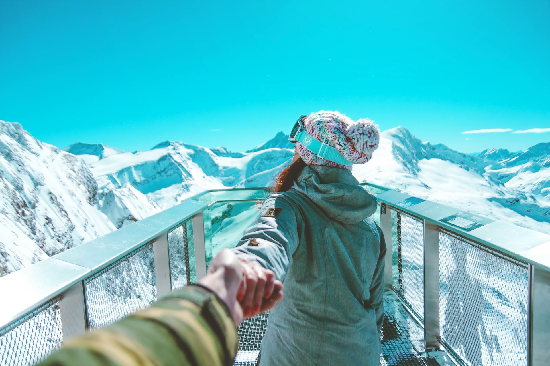 A woman is holding a man 's hand while standing on a balcony overlooking snow covered mountains.