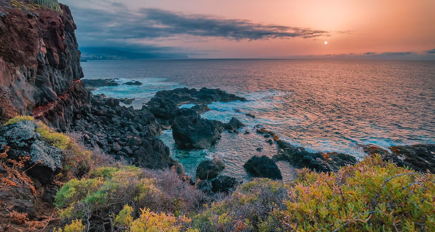 A sunset over the ocean with a rocky shoreline in the foreground.