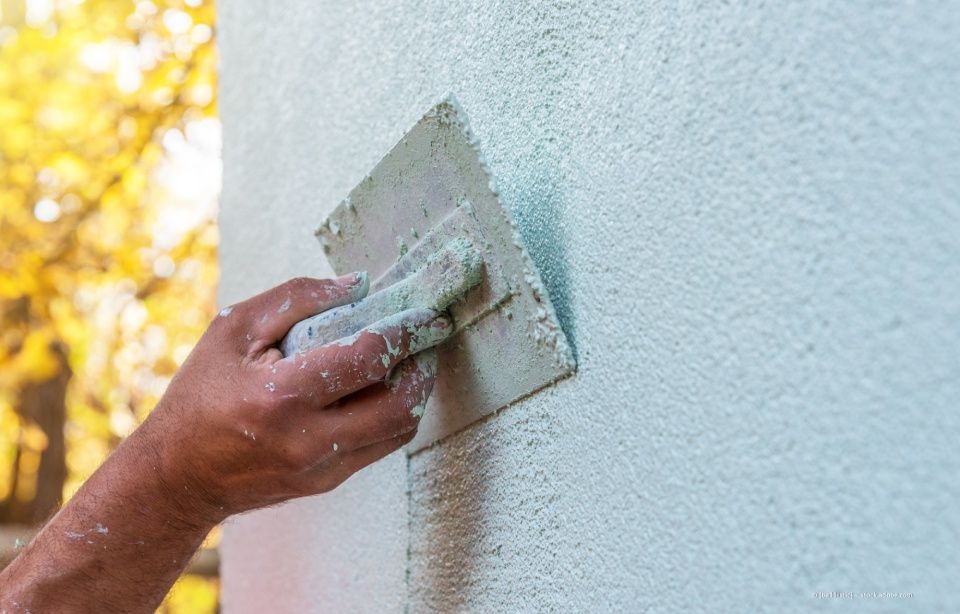 Hellblauen Stuck mit einer Kelle von Hand an einer Außenwand glätten.