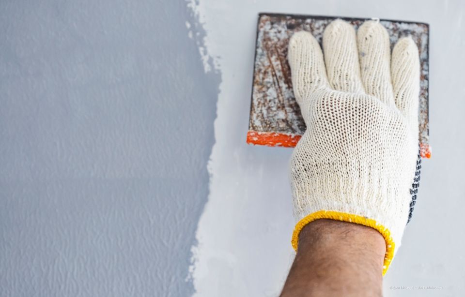 Person, die eine Wand mit einem Schleifblock schleift und dabei einen Arbeitshandschuh trägt.