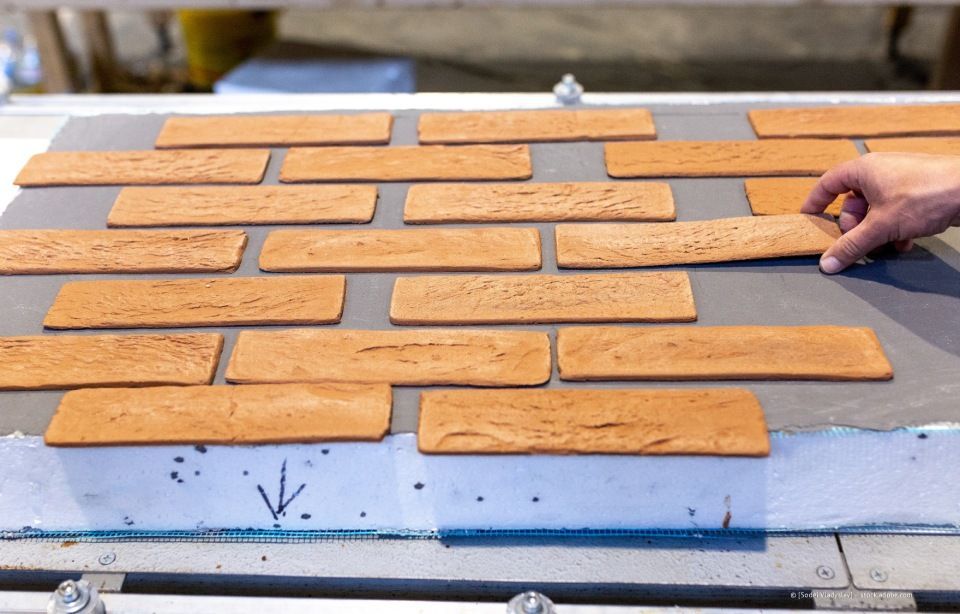 Eine Hand legt einen braunen Ziegelstein auf eine gemusterte Ziegelsteinschicht, ein Herstellungsprozess.