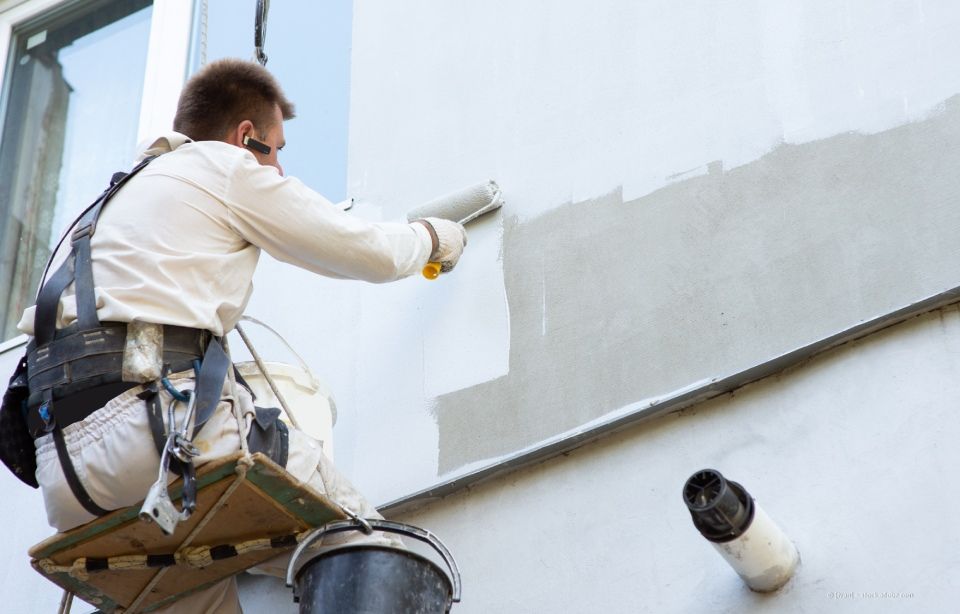 Maler auf Gerüst, streicht Außenwand grau.