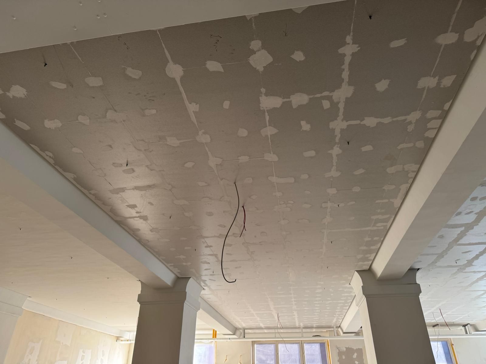 Person mit Handschuhen, die mit einem Spachtel Spachtelmasse auf eine Wand aufträgt.