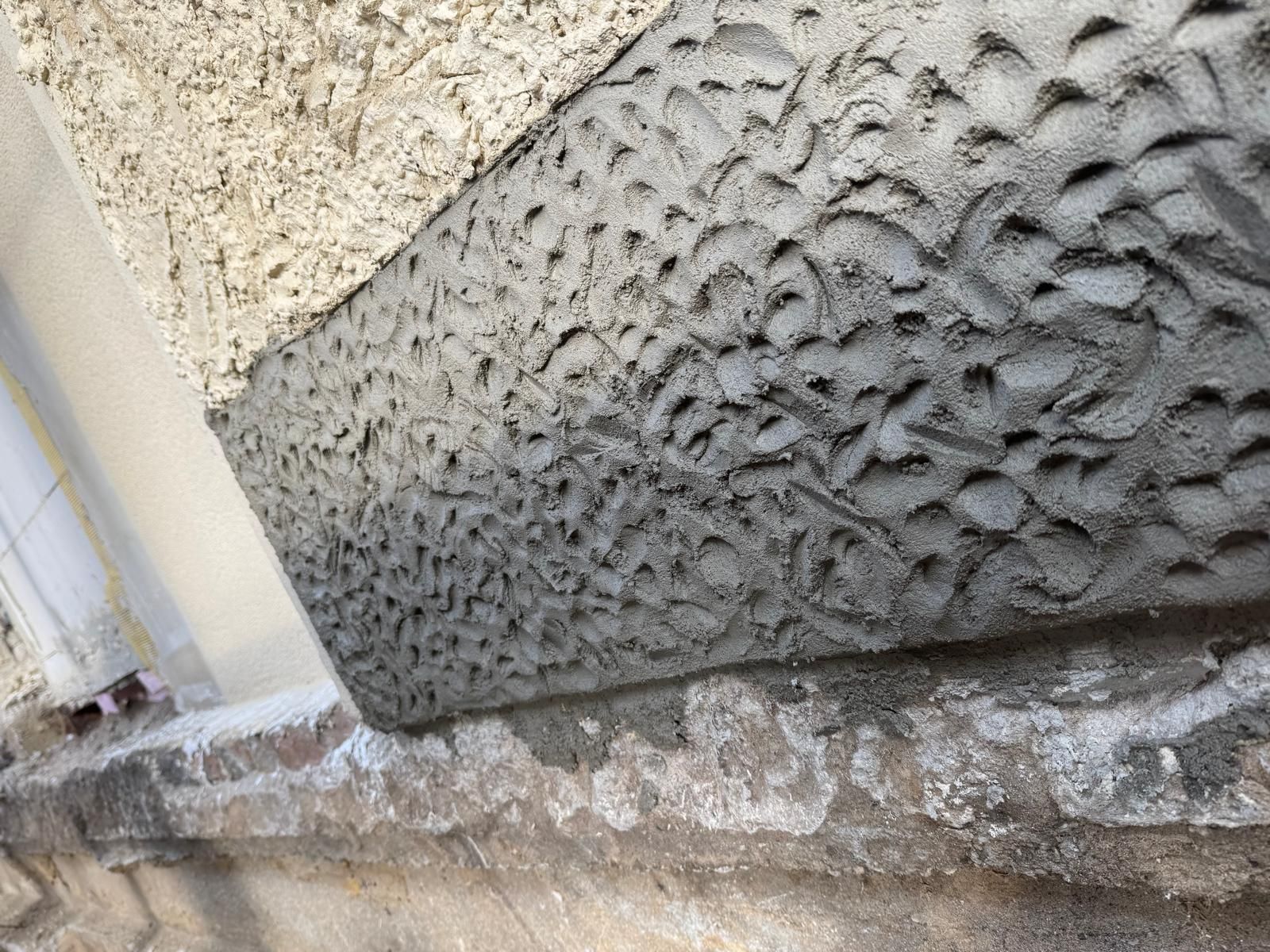 Person mit roten Handschuhen hält ein Spachtelmesser mit weißer Spachtelmasse und arbeitet an einer weißen Wand.