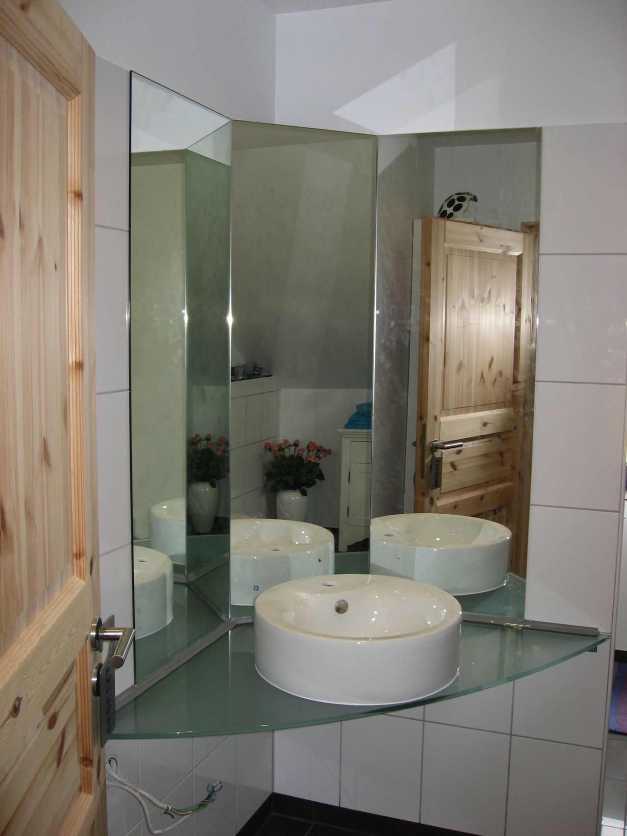 Ein Badezimmer mit einem Eckwaschbecken drei Spiegeln und Glaskonstruktion