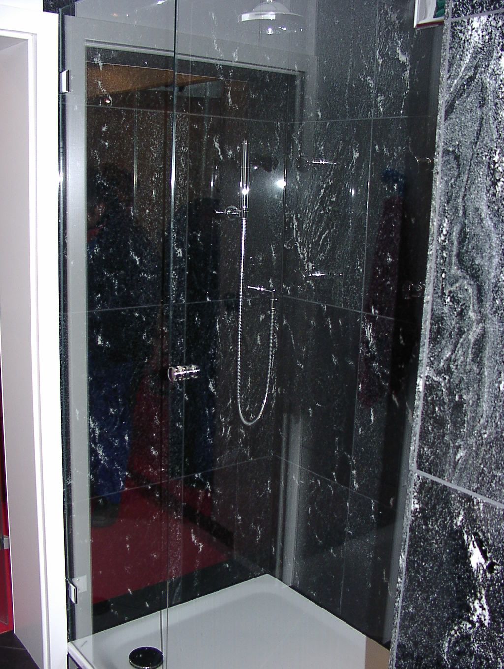 Ein Badezimmer mit schwarzen Fliesen und einer Glasduschtür