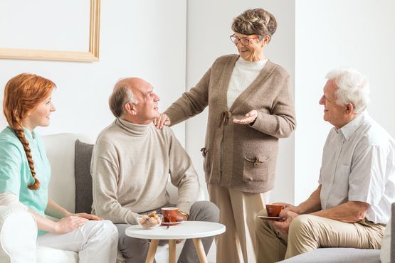 Un cuidador y tres personas conversan sentadas en una habitación luminosa y moderna mientras disfrutan de un café.