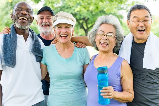 Un grupo diverso de cinco personas sonriendo juntas al aire libre, vestidas con ropa deportiva, con toallas y una botella de agua.