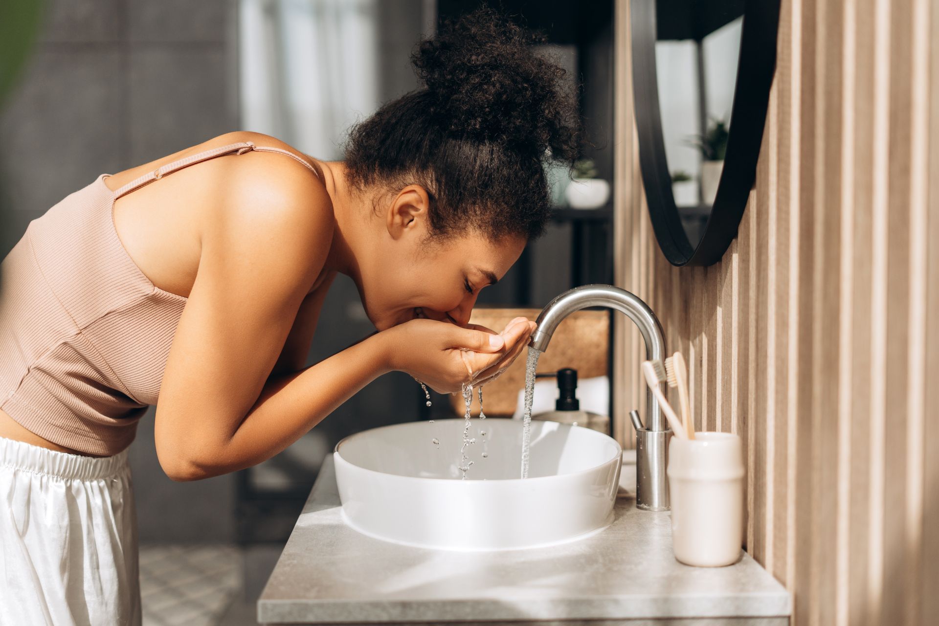 Une femme penchée au-dessus du lavabo de la salle de bains se rince le visage à l'eau du robinet.