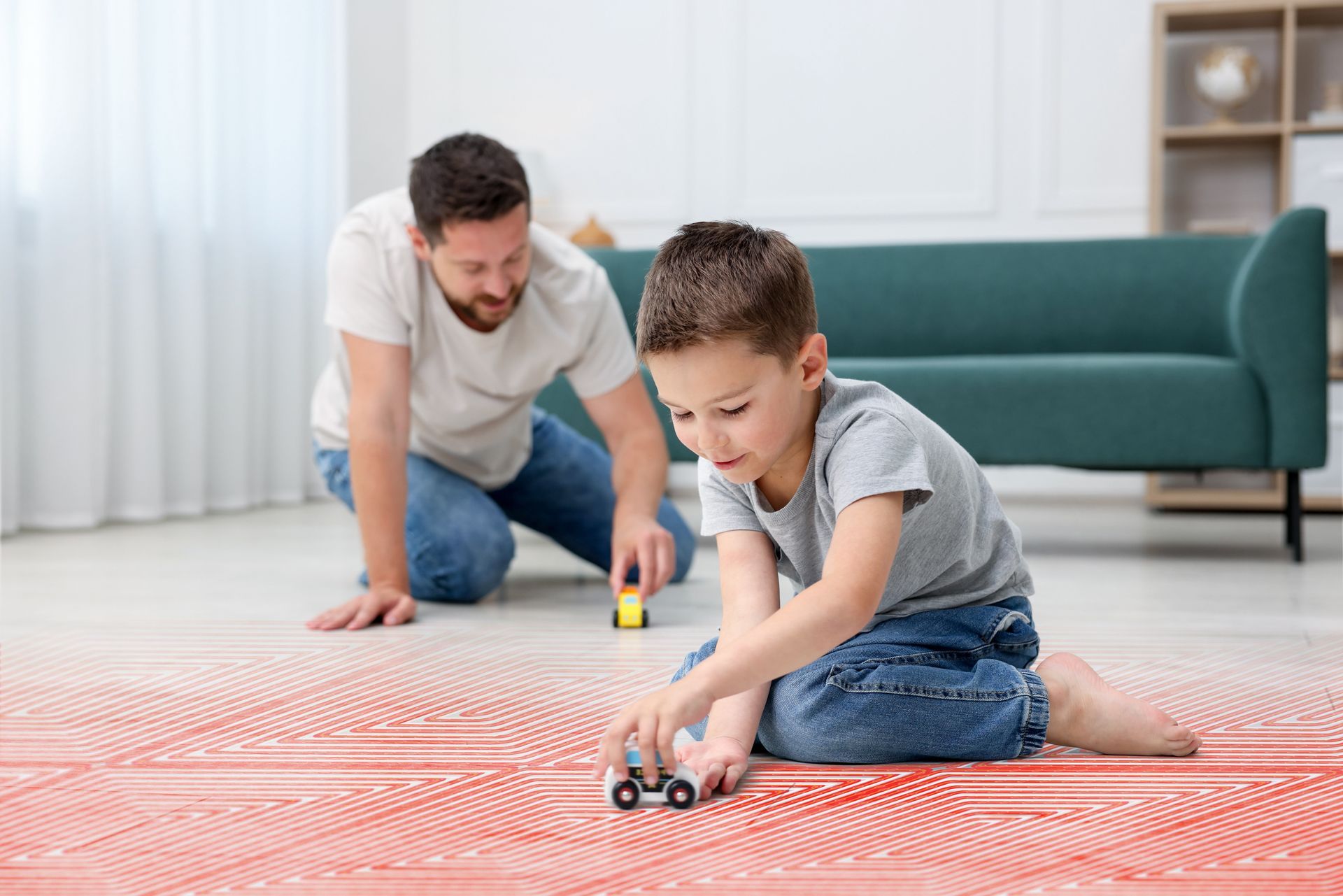 Un homme et un enfant jouent avec des petites voitures sur un tapis rouge dans un salon lumineux.