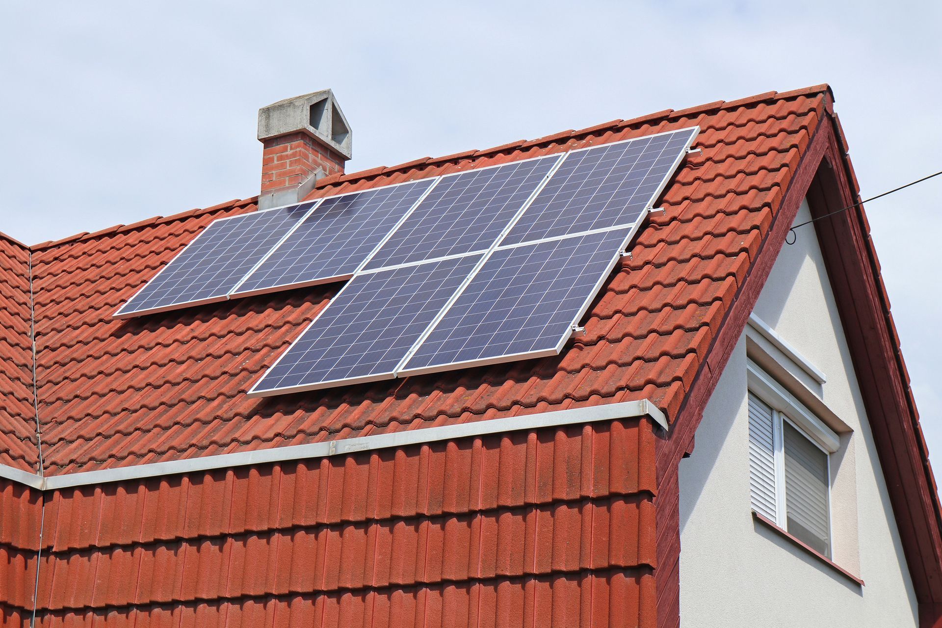 Des panneaux solaires sur le toit d'une maison aux tuiles rouges, sous un ciel bleu.