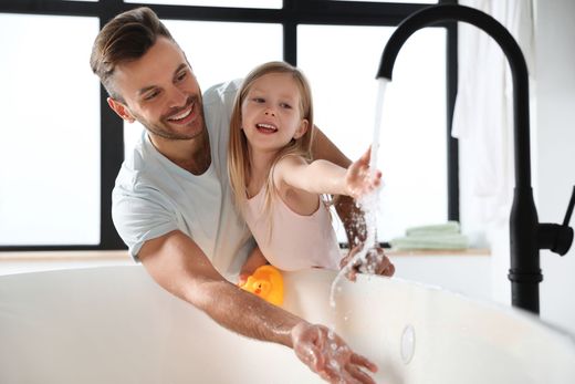 Un homme et un enfant sourient en se lavant les mains à un lavabo avec de l'eau courante.