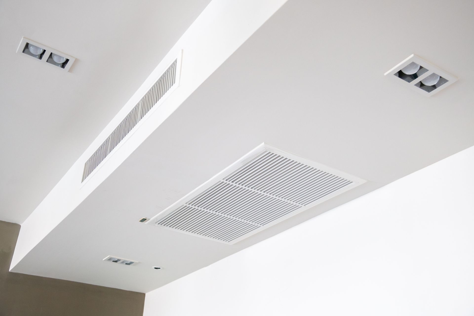Plafond blanc avec aérations et éclairage encastré dans un intérieur moderne.