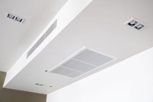 Plafond blanc avec aérations et éclairage encastré dans un intérieur moderne.