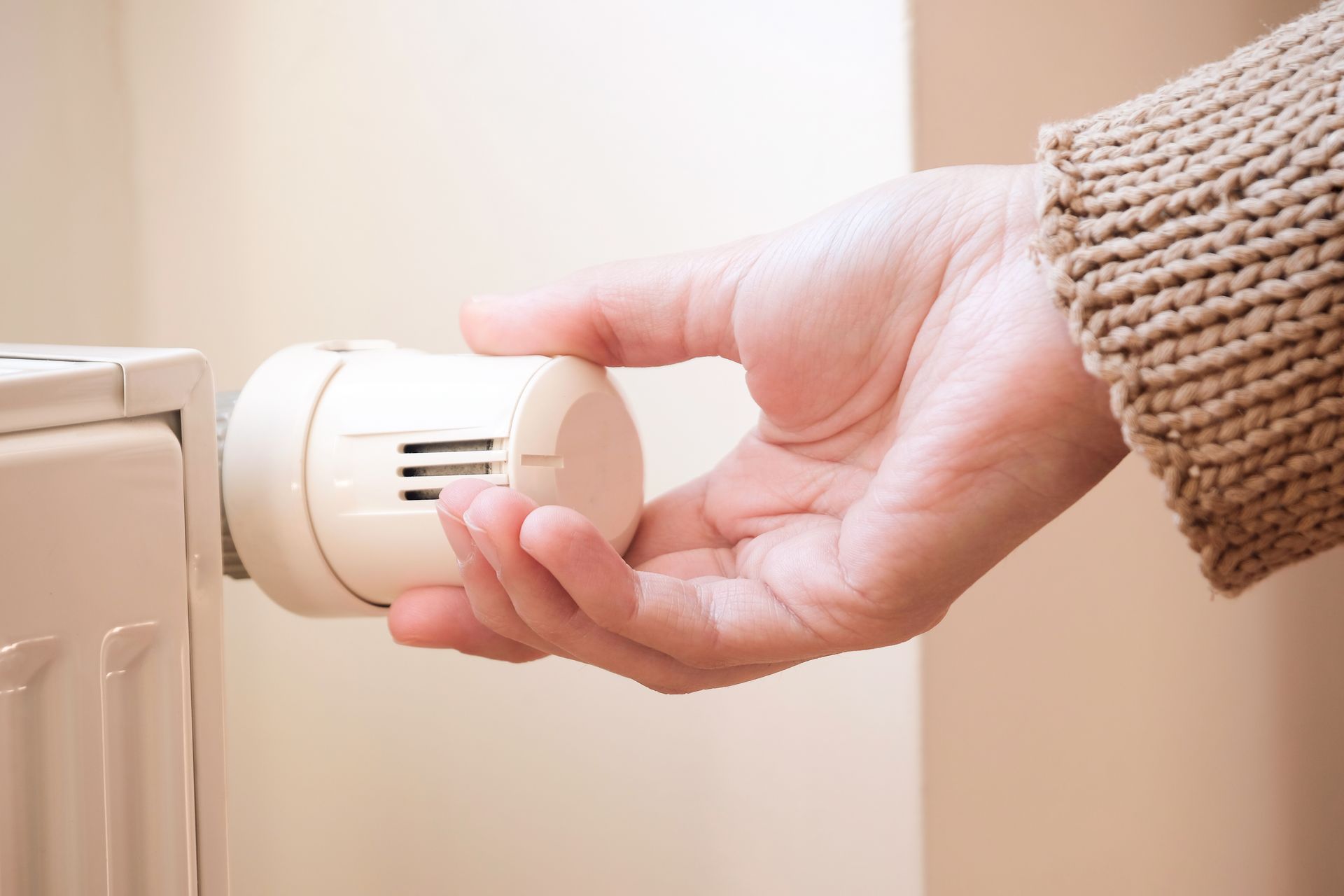Main tournant le bouton blanc du thermostat d'un radiateur à l'intérieur.