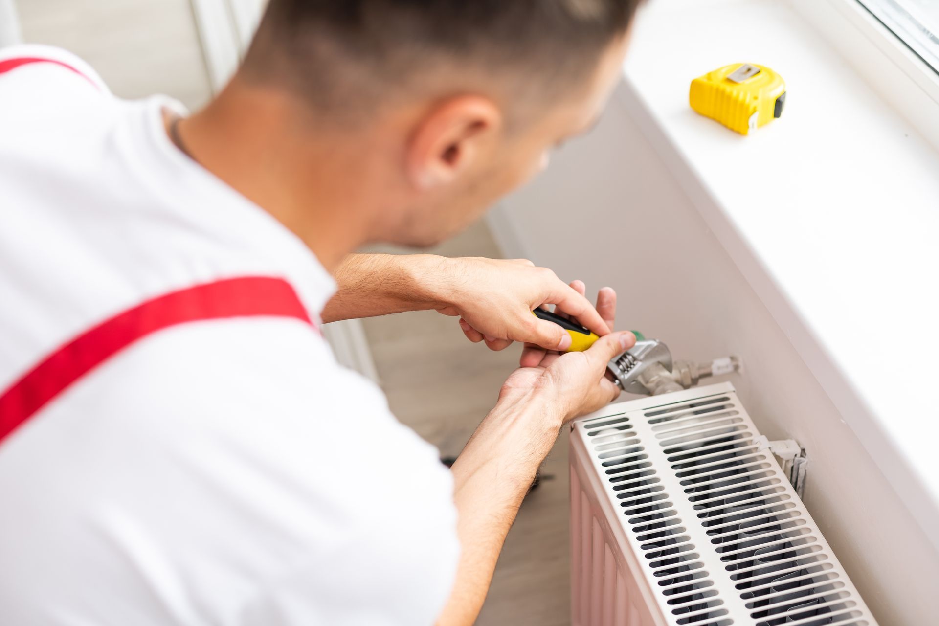Un technicien règle le thermostat d'un radiateur avec un tournevis dans une pièce lumineuse.