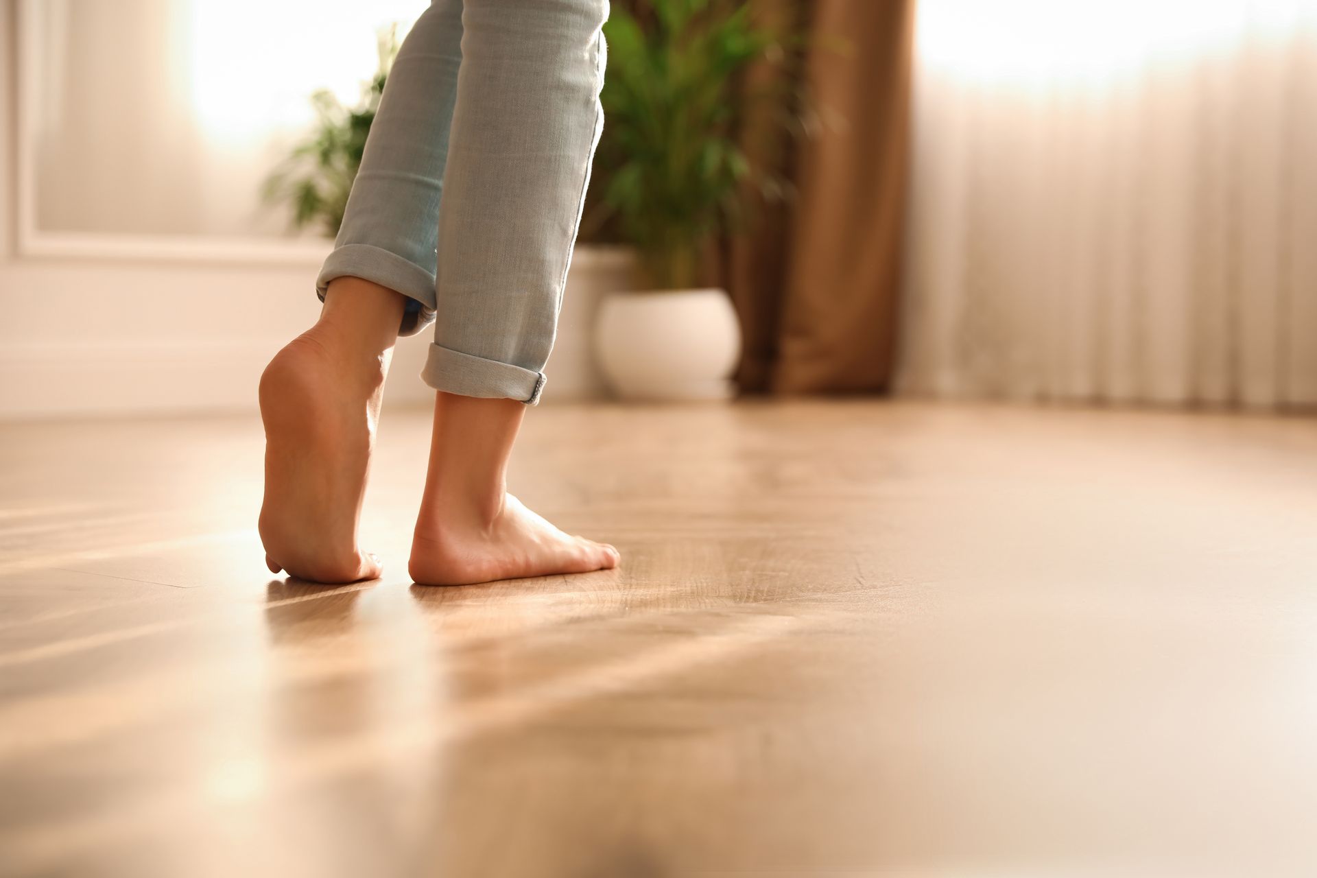 Des pieds nus marchant sur un plancher de bois dans une pièce ensoleillée.