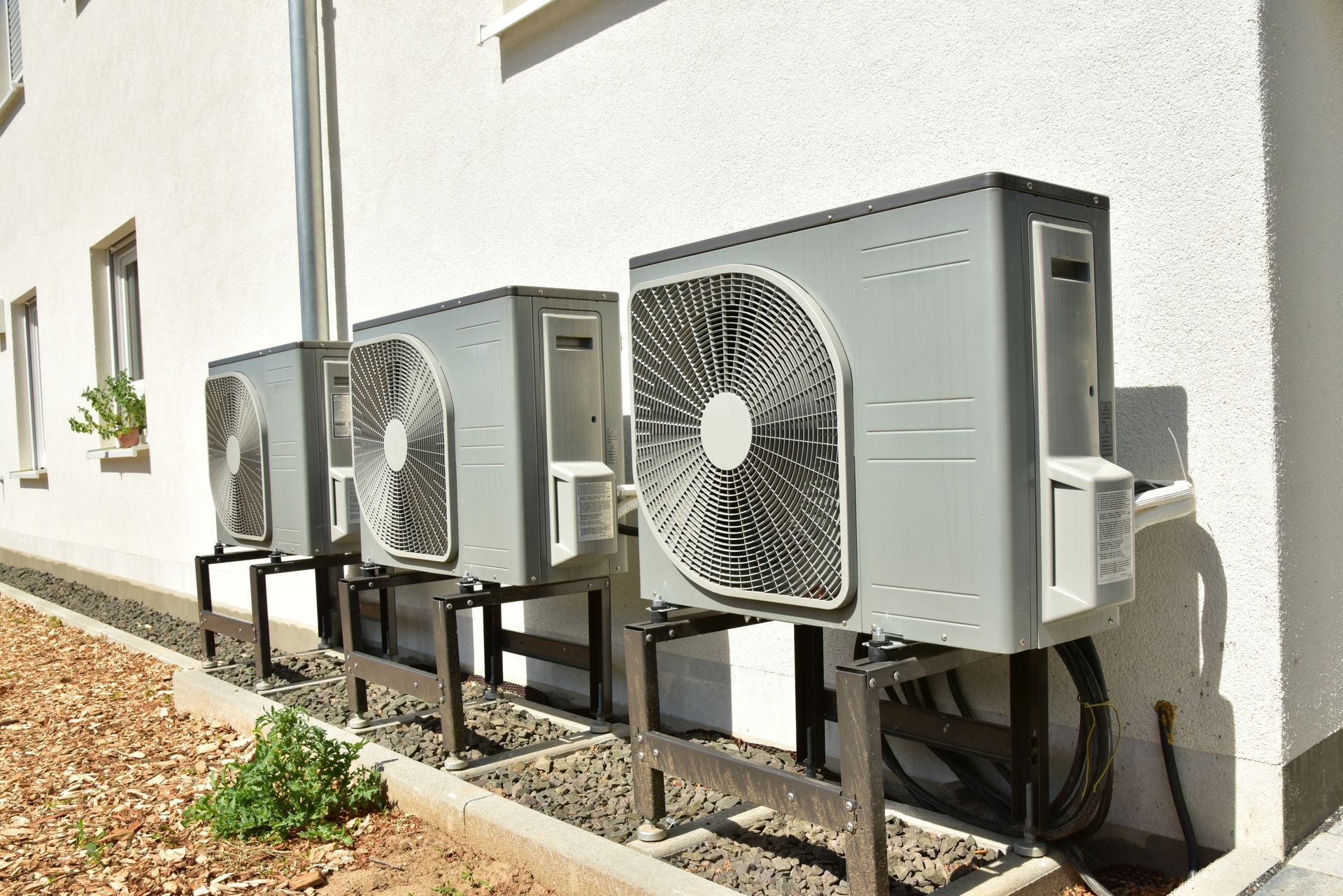 Rangée d'unités de climatisation extérieures à côté d'un bâtiment blanc sur du gravier.