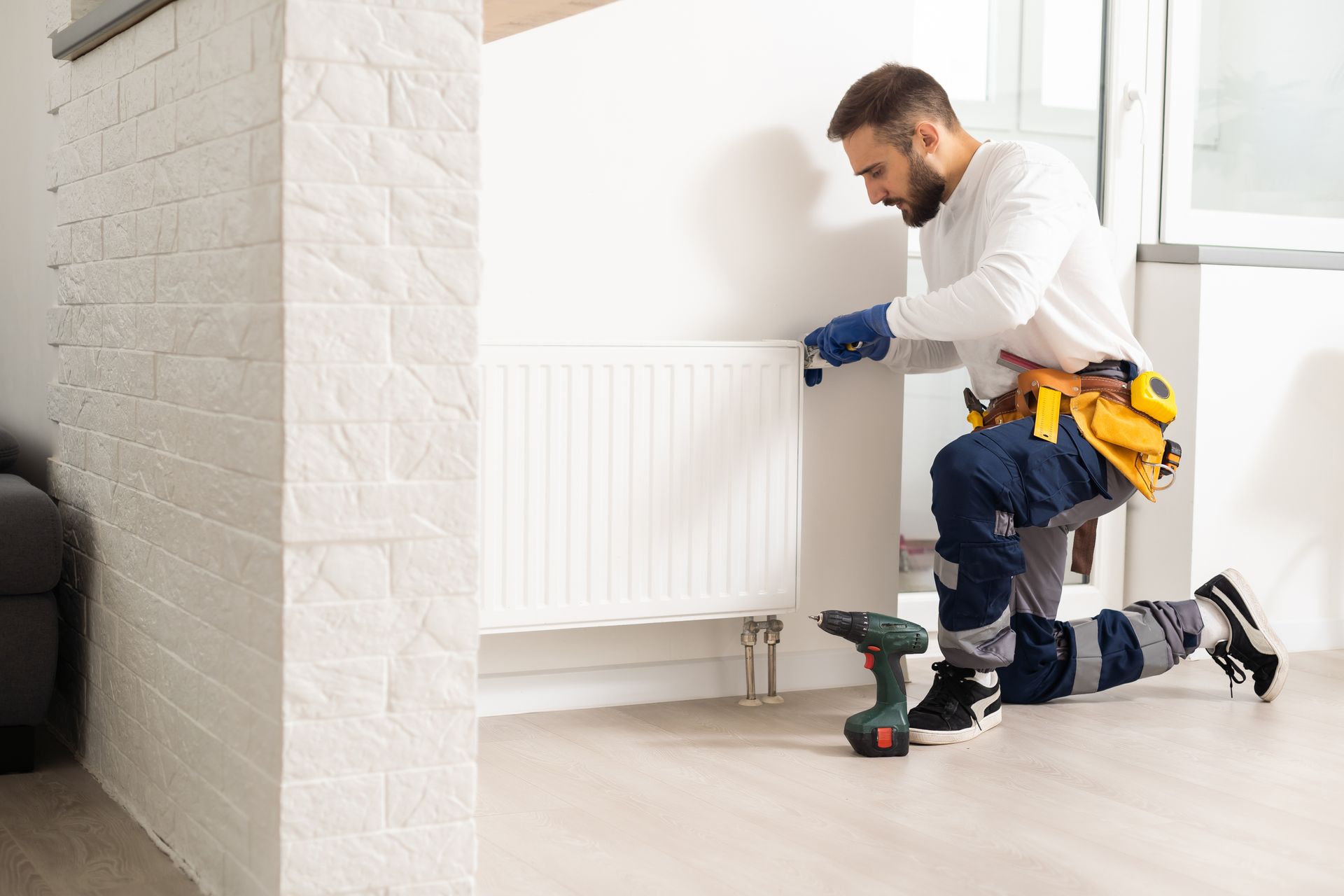 Un technicien installe un radiateur mural blanc avec ses outils dans une pièce lumineuse.