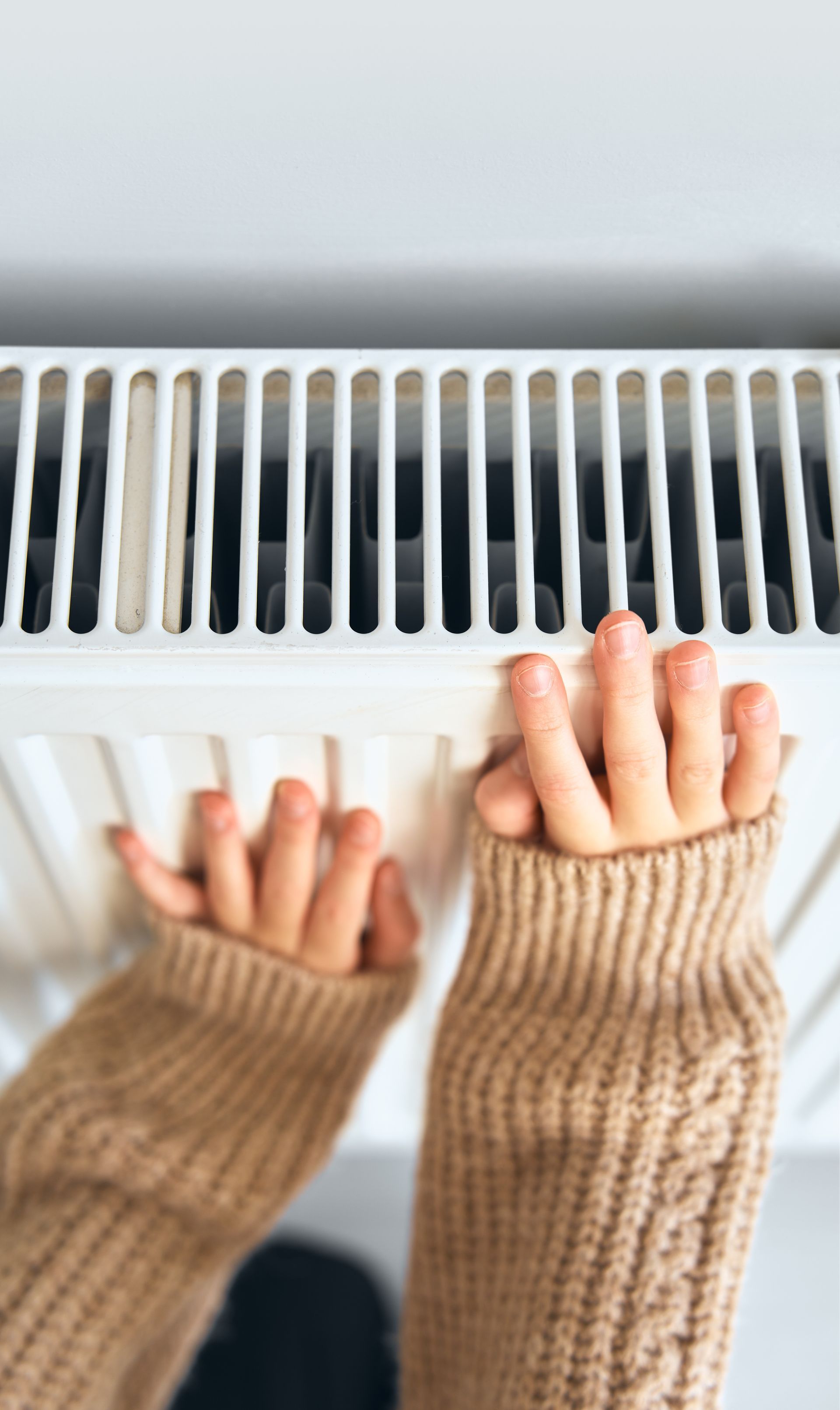Des mains se tendent vers une grille d'un radiateur blanc.