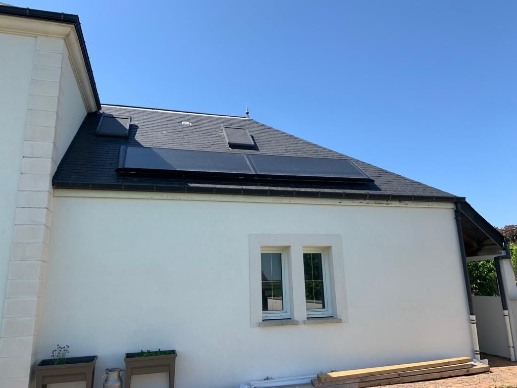 Mur blanc d'une maison avec une petite fenêtre et des panneaux solaires sur le toit, sous un ciel bleu clair.