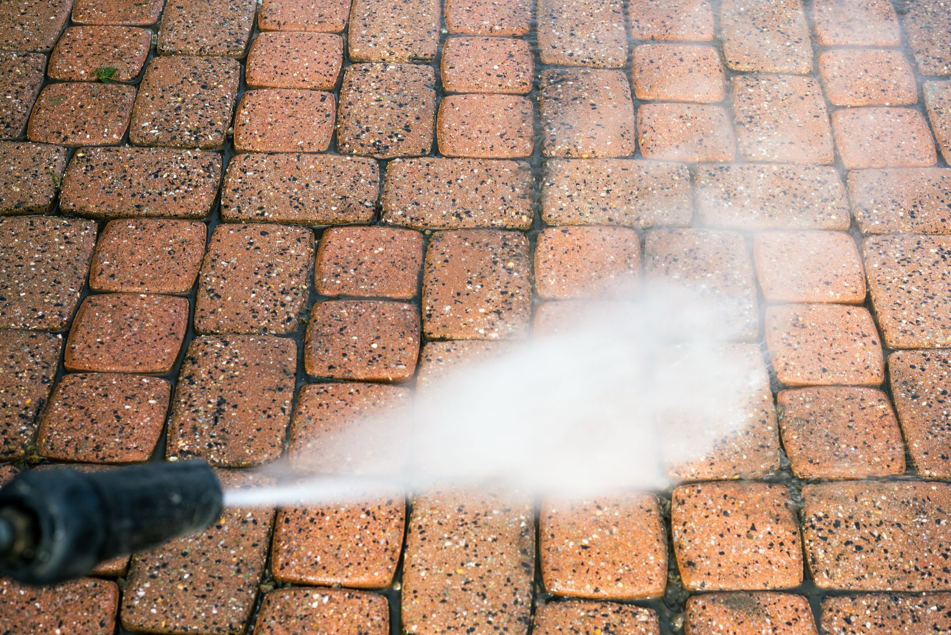 Nettoyeur à haute pression pulvérisant de l'eau sur des pavés.