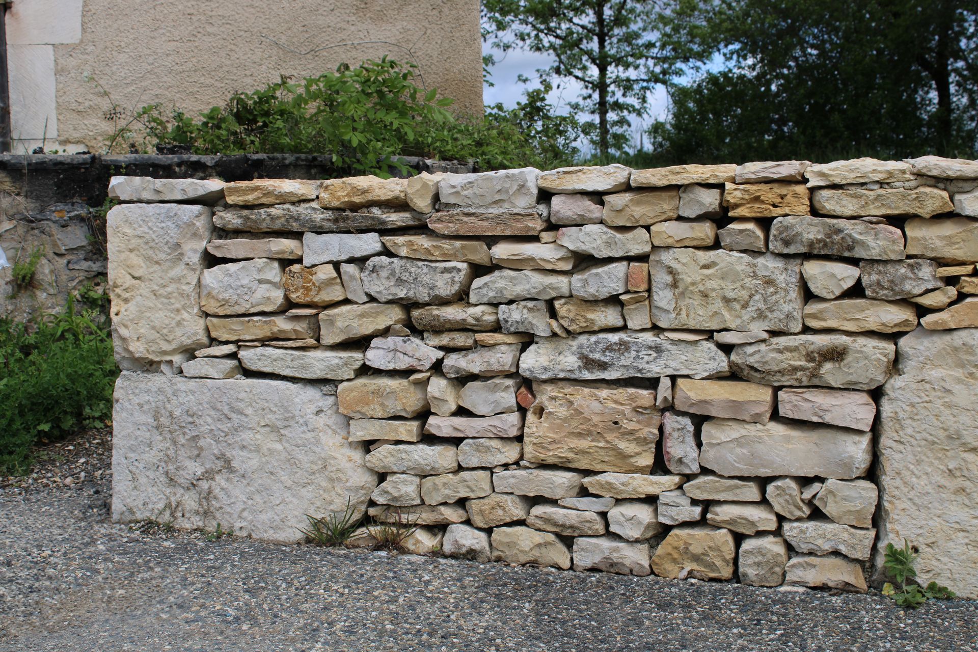 Mur en pierre composé de blocs de différentes tailles, adjacent à un bâtiment, avec de grands piliers de pierre à chaque extrémité.