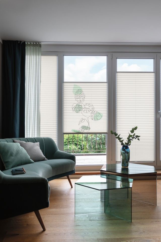 Wohnzimmer mit türkisfarbenem Sofa, Couchtisch aus Glas und Plissees.