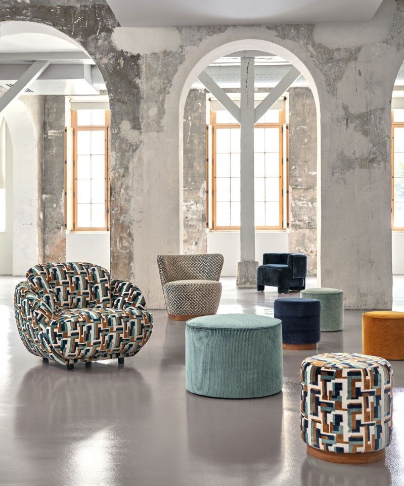 Eine Sammlung gemusterter Sessel und Hocker in einem Raum im Used-Look mit Industrie-Flair.