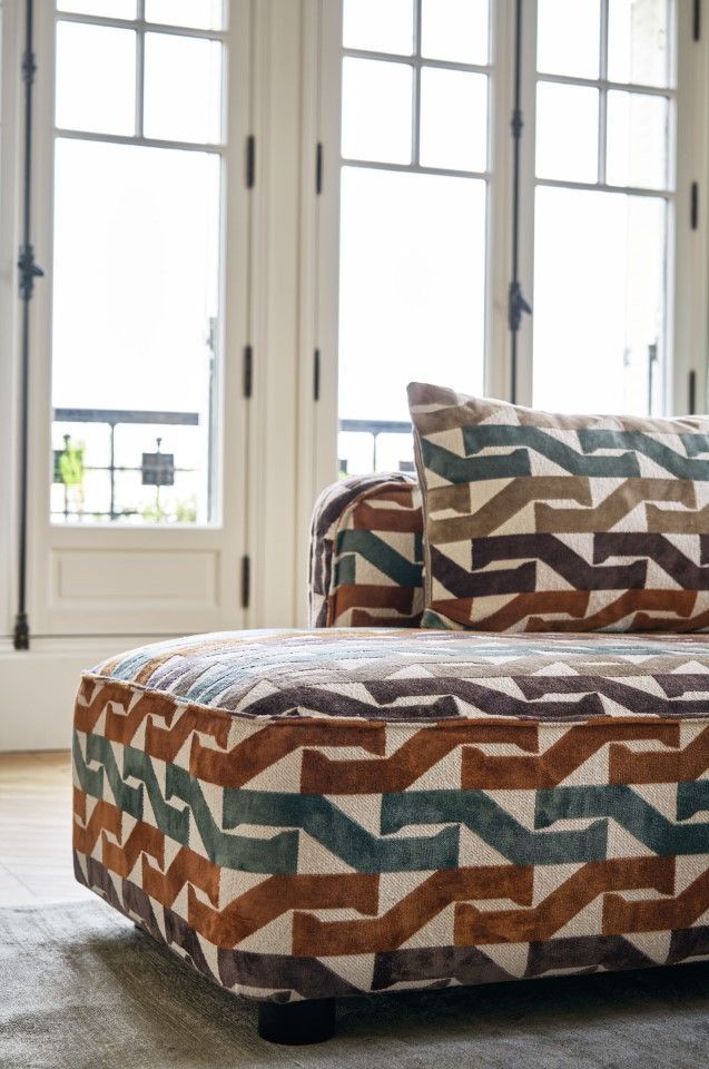 Sofa mit geometrischem Muster und großem Kissen, in der Nähe eines hellen Fensters.