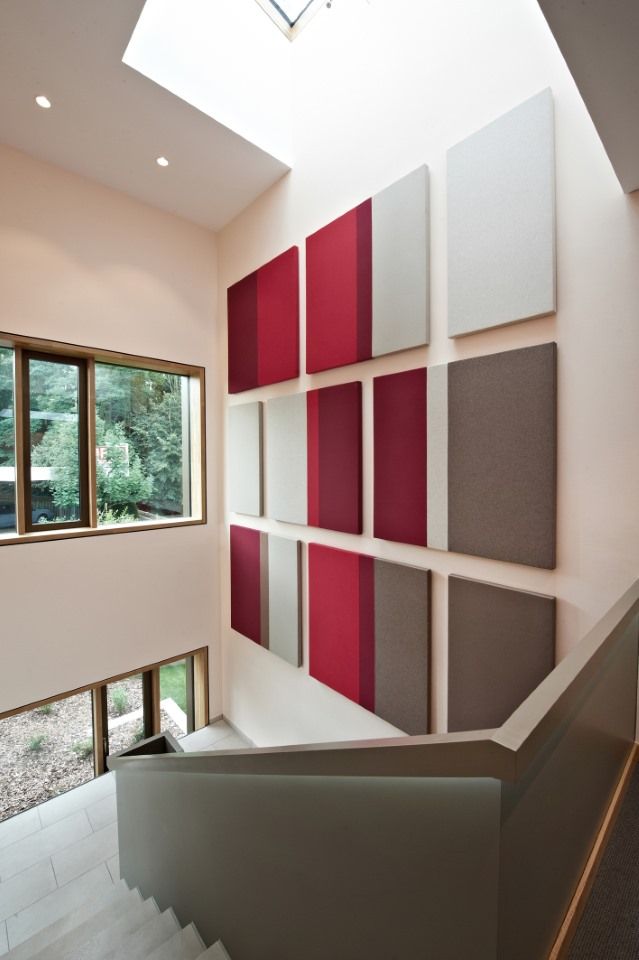 Treppenhaus mit modernen Kunstpaneelen in Rot, Grau und Weiß an einer hellen Wand, mit natürlichem Licht durch ein Oberlicht.