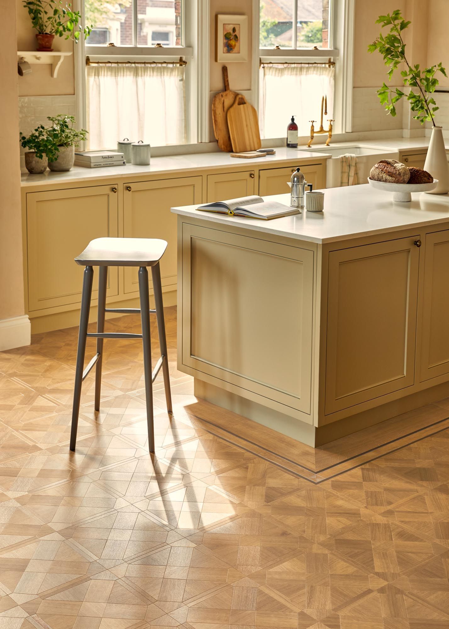 Küche mit Kochinsel, hellen Holzschränken und gemustertem Holzboden. Sonnenlicht strömt durch die Fenster.