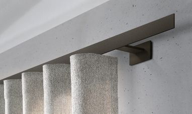 Nahaufnahme einer Gardinenstange mit beigefarbenen Gardinen vor einer hellgrauen Wand. Die Stange ist dunkelbraun.