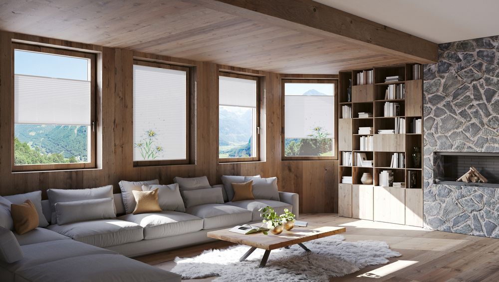 Gemütliches Wohnzimmer mit grauer Eckcouch, Holzelementen, Steinkamin, großen Fenstern mit Bergblick und eingebautem Bücherregal.