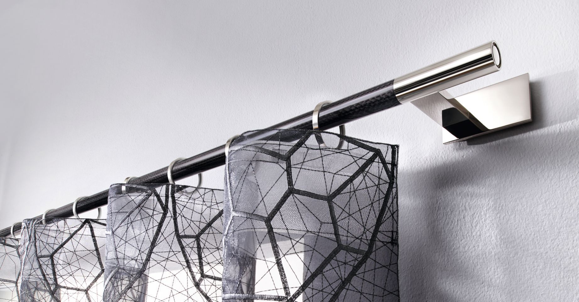 Schwarze Gardinenstange mit geometrischen Mustervorhängen, montiert an einer weißen Wand.