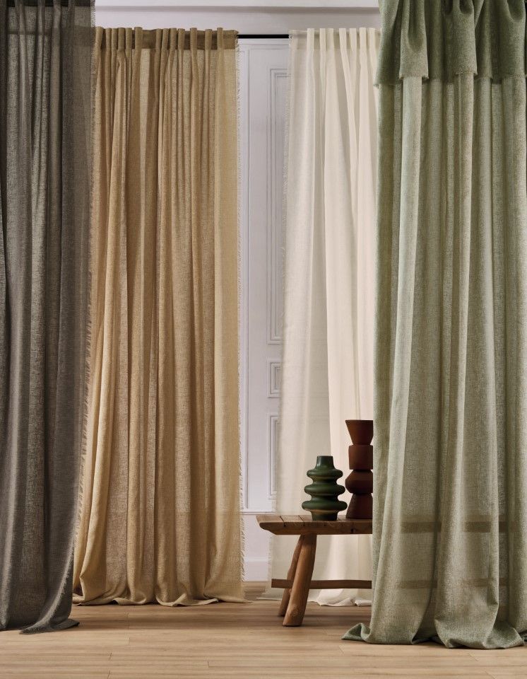 Vier hauchdünne Vorhänge in verschiedenen neutralen Farbtönen hängen vor einem Fenster.