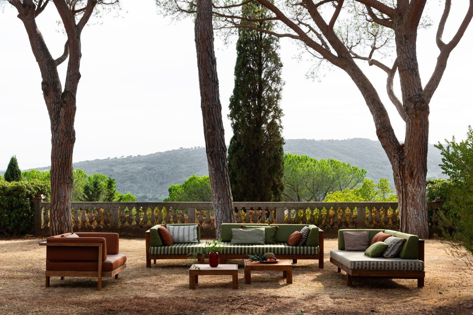 Sitzbereich im Freien mit Sofa, Stühlen und Couchtischen auf Kiesfläche, umgeben von Bäumen und mit malerischem Ausblick.