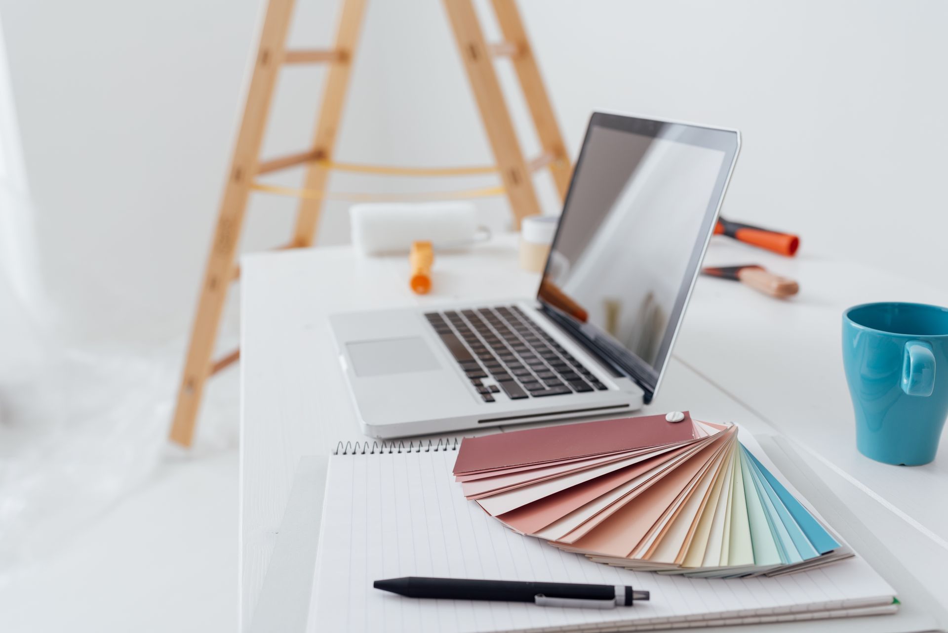 Dans une pièce en cours de rénovation, un ordinateur et des échantillons de peinture sont posés sur une table.