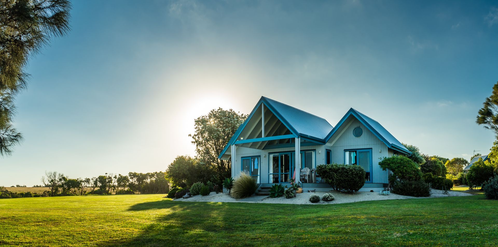 Une maison ensoleillée avec une véranda sur une pelouse verte.