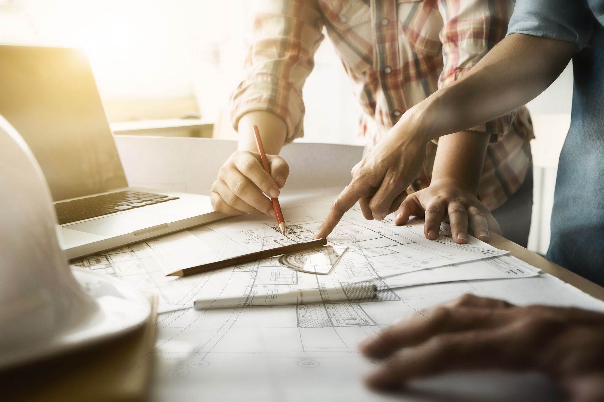 Des professionnels du bâtiment dessinent des plans de construction à côté d'un ordinateur portable.